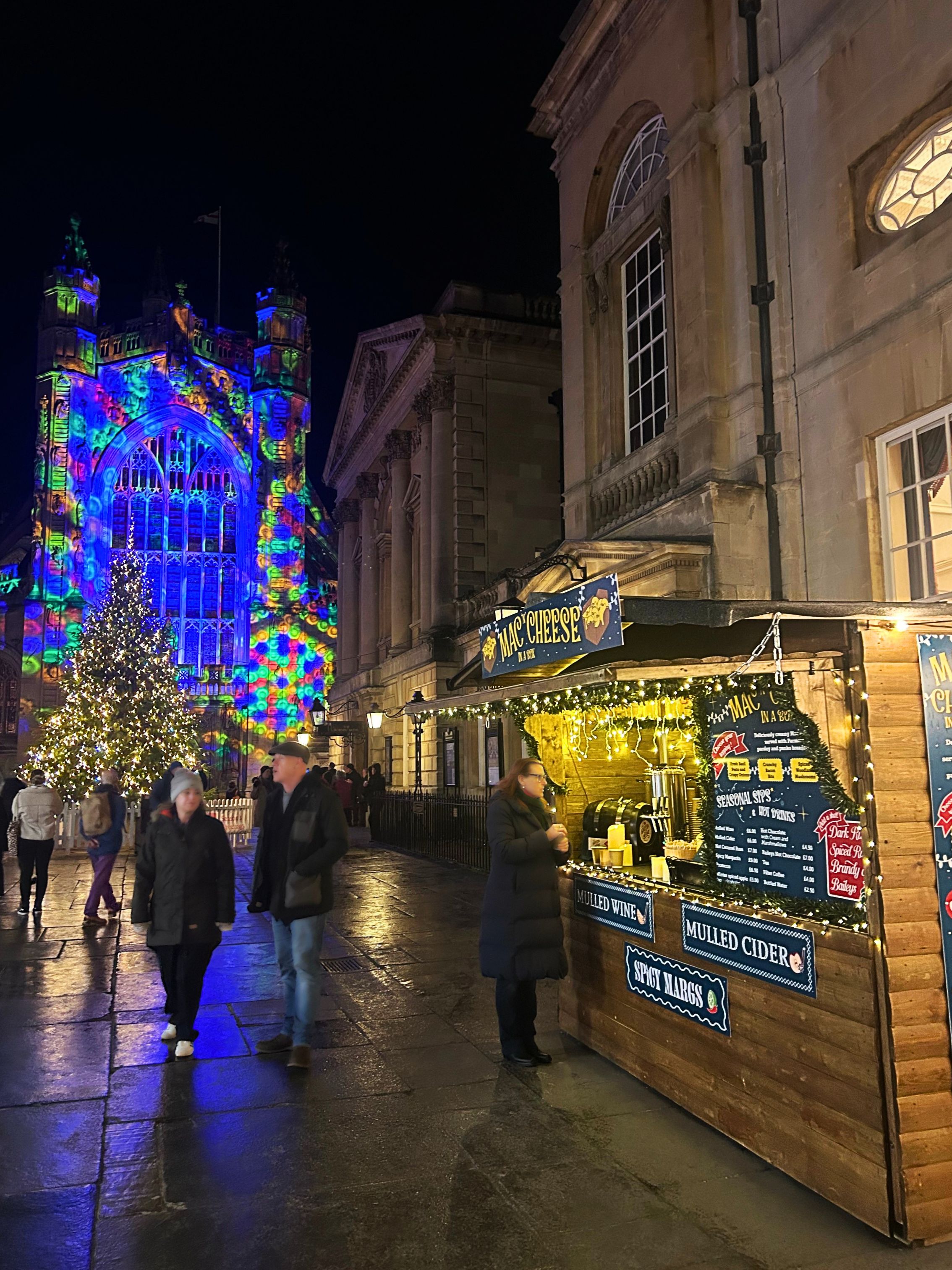 One of the Bath Christmas Market chalets, serving Mac and Cheese, in front of the Bath Abbey Christmas tree and lights.